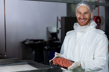Man placing black tray of raw burger patties on stainless steel table inside meat processing plant