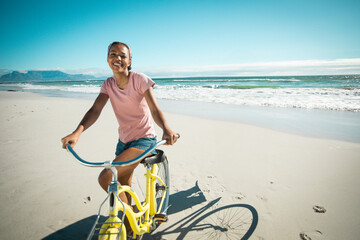 African American woman riding yellow cruiser bicycle on sandy beach, smiling against ocean waves