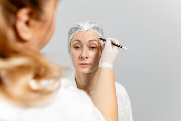 Close-up. Before the procedure for facial contouring or plastic surgery, the cosmetologist makes...