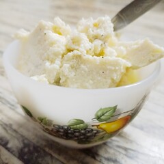 Creamy Kharvas in a white bowl with fruit motifs, topped with cardamom specks. Made from colostrum milk, this chilled Indian sweet has a soft, grainy texture and rich flavor.