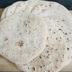 A stack of soft, freshly made rotis with golden brown spots, placed on a wooden board. These Indian flatbreads are perfect for pairing with curries or dry dishes in any traditional meal.