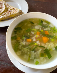 A bowl of soup with green vegetables and a piece of bread on a plate