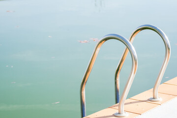 shiny metal handrails of a swimming pool ladder, detail with visible murky water surface