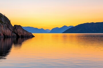 A serene sunset over calm waters, reflecting vibrant orange and yellow hues, surrounded by rugged mountains and cliffs.