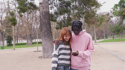 Interracial couple sharing joyful moment while browsing smartphone screen during park walk, radiating connection and happiness together - Powered by Adobe