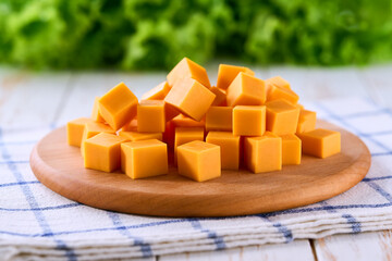 Cubes of cheddar cheese on a white wooden table, selective focus.