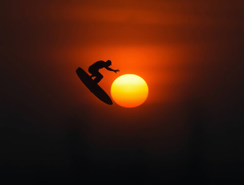 a surfer in mid-air against a vibrant sunset backdrop. The layout is horizontal, emphasizing the expansive ocean and sky. The subject, a silhouette of a person, is performing an aerial maneuver on a s