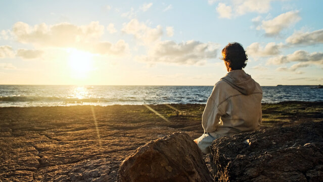 Man on a beach is looking distance during beautiful summer sunset. Human looks to the sun over horizon in the morning while sunrise. Happy person contemplates the beauty of nature. Freedom concept.