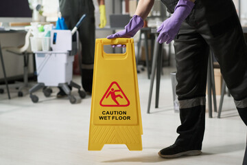 Close-up of worker in uniform using caution board during cleaning in office