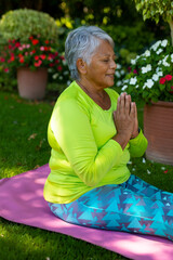 Senior woman practicing yoga on pink yoga mat in garden, with terracotta pots holding prayer pose