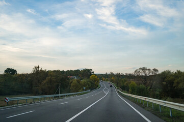 Winding country road invites adventure under a serene sky, surrounded by lush greenery and hints of autumn colors