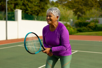 Senior woman standing ready on tennis court, holding racket, wearing smartwatch, copy space