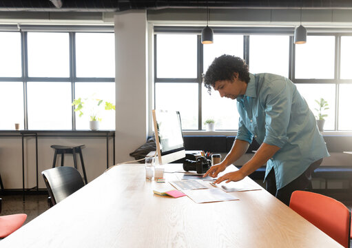 Young multiracial man reviewing documents at office conference table, with DSLR camera, copy space
