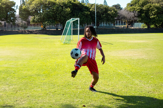 male soccer player juggling black-and-white ball on soccer field at green goal net, showing skill - Powered by Adobe