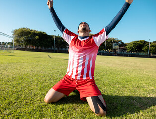 Teenage boy kneeling on soccer field by goalpost, celebrating goal with tape on knee