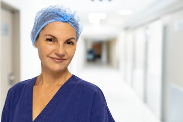 Female nurse standing and smiling in hospital corridor, wearing navy-blue scrub top and hairnet