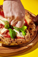 Chef cutting neapolitan pizza with wheel cutter on yellow background
