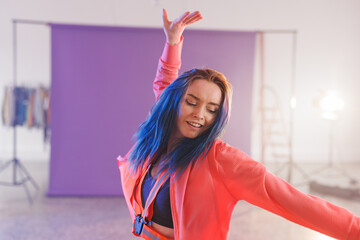 Non-binary young adult dancing in photography studio with purple backdrop and action camera harness © WavebreakMediaMicro