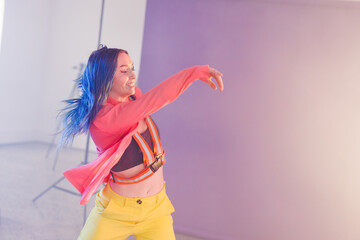 Non-binary dancer dancing in indoor photography studio, wearing orange harness with lighting stand