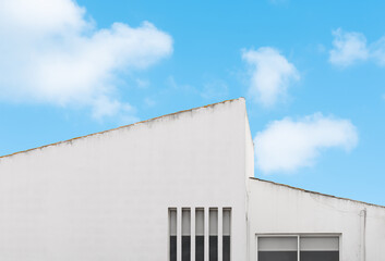 White concrete wall building with light and shadow against clear blue sky, cloud background,Minimal style perspective side view striking architectural corner detail of angle roof in geometric triangle