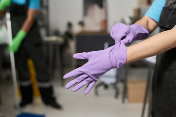 Close-up of cleaner wearing rubber gloves for work in office