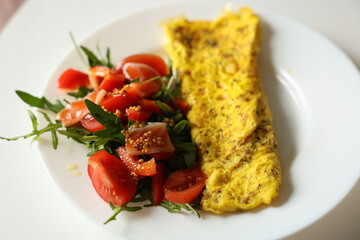 Healthy breakfast with omelette and fresh salad with cherry tomatoes and arugula, dressed with mustard, honey and olive oil sauce on white plate. Nutritious meal with protein and fiber. Ketogenic diet