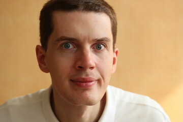Young man face with dark hair on a light brown background.