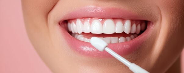Naklejka premium A close-up of a smiling mouth showcasing bright white teeth, with a cotton swab being used on the gums against a soft pink background.
