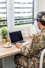 Fototapeta premium vertical Soldier studying using laptop and book at home