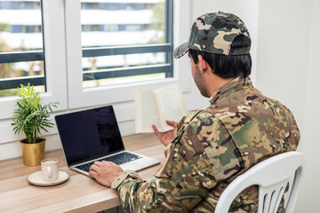 Fototapeta premium Soldier studying using laptop and reading book at home