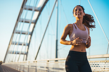 Smiling Woman Jogging on a Bridge Under a Clear Sky at Sunset
