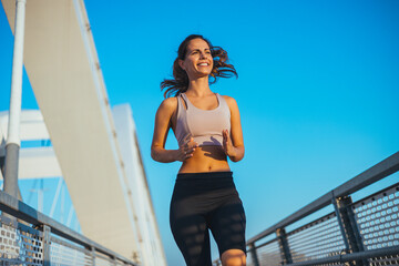 Fototapeta premium Young Woman Jogging on a Bridge During a Sunny Day