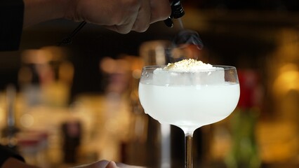 Closeup hand bartender using strainer in vodka coconut smooth fizzy cocktail at luxurious counter...