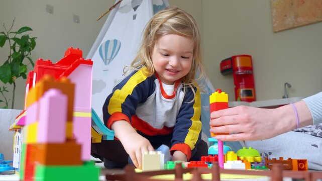 A young child and mother playing with colorful building blocks in a cozy indoor setting. Warm family bonding, creativity, and childhood development in a playful and loving home environment.