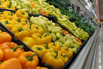 A colorful display of orange, yellow bell peppers and chili peppers fills a supermarket produce aisle