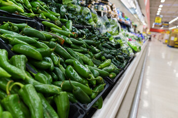 A supermarket produce section showcasing a bountiful display of fresh jalapeño and poblano peppers