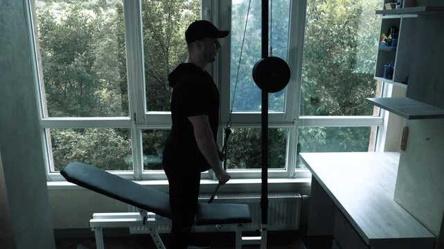 Pumping triceps arms on a sports simulator in an apartment at home. A young man trains his triceps by doing rope rows.
