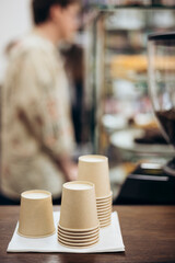 A lot of disposable paper cups near coffee machine with coffee shop background.