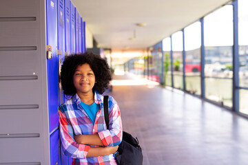 African American child boy leaning against blue lockers in corridor, carrying backpack, copy space