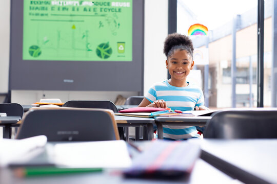 girl student sitting at classroom desk, viewing recycling slide, using colored pencils