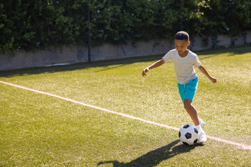 African American child dribbling soccer ball on grassy field near boundary line, copy space