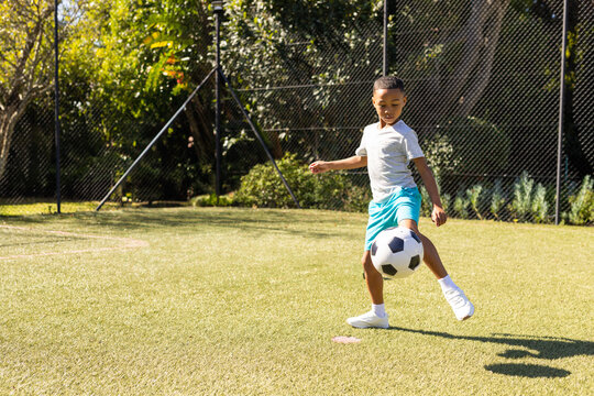 African American boy balancing soccer ball on artificial turf field with mesh fence, copy space - Powered by Adobe