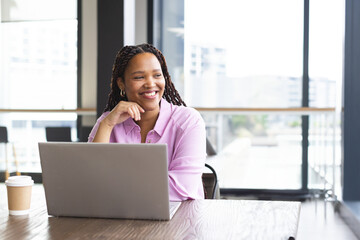 Woman sitting at table in modern office working on silver laptop with coffee cup, copy space