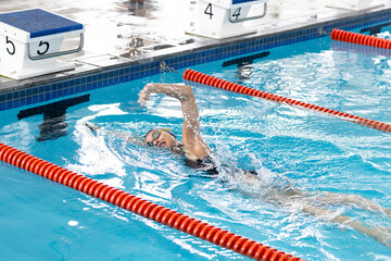 Teenage female swimmer performing backstroke in pool lane, wearing yellow cap and goggles