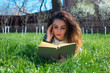 Fototapeta premium Beautiful girl lies on meadow and reads the book
