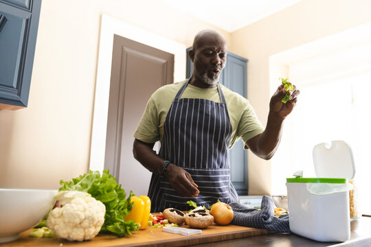 Senior African American man chopping vegetables in home kitchen, with mixing bowl, compost bin - Powered by Adobe