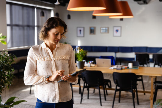 Woman standing and holding tablet at modern coworking office, with laptop mug stylus and plants