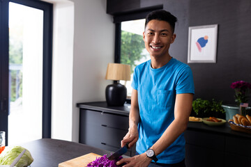 Asian man chopping purple cabbage on kitchen island in modern home, using chef's knife