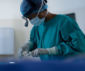 African American female surgeon leaning over patient in surgery room holding forceps and retractor
