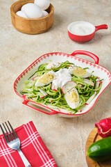 Spring cucumber and radish salad with boiled egg and sour cream dressing in a deep plate on a light concrete background. Vegetarian recipes.